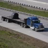 Picture of a blue flatbed trailer covering its cargo with a coil tarp on a sunny day.