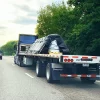 Blue flatbed trailer driving next to green trees depicting the use of 16x27 steel tarp