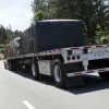 Picture of a brown flatbed trailer showing the application of black lumber tarp 4 drop.