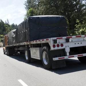 Picture of a brown flatbed trailer showing the application of black lumber tarp 4 drop.