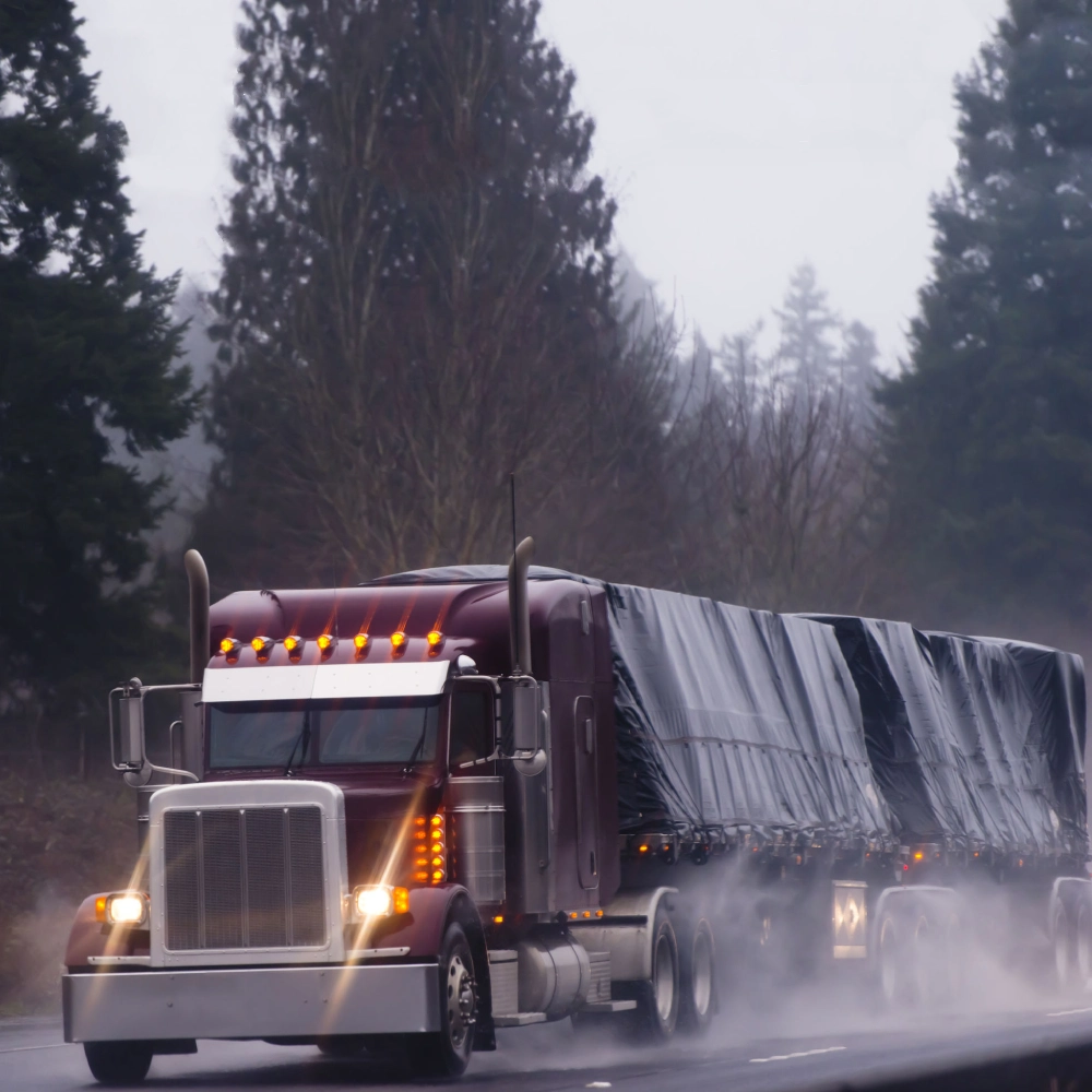 Picture of a burgundy trailer with two 6 drop lumber tarps on a wet road.