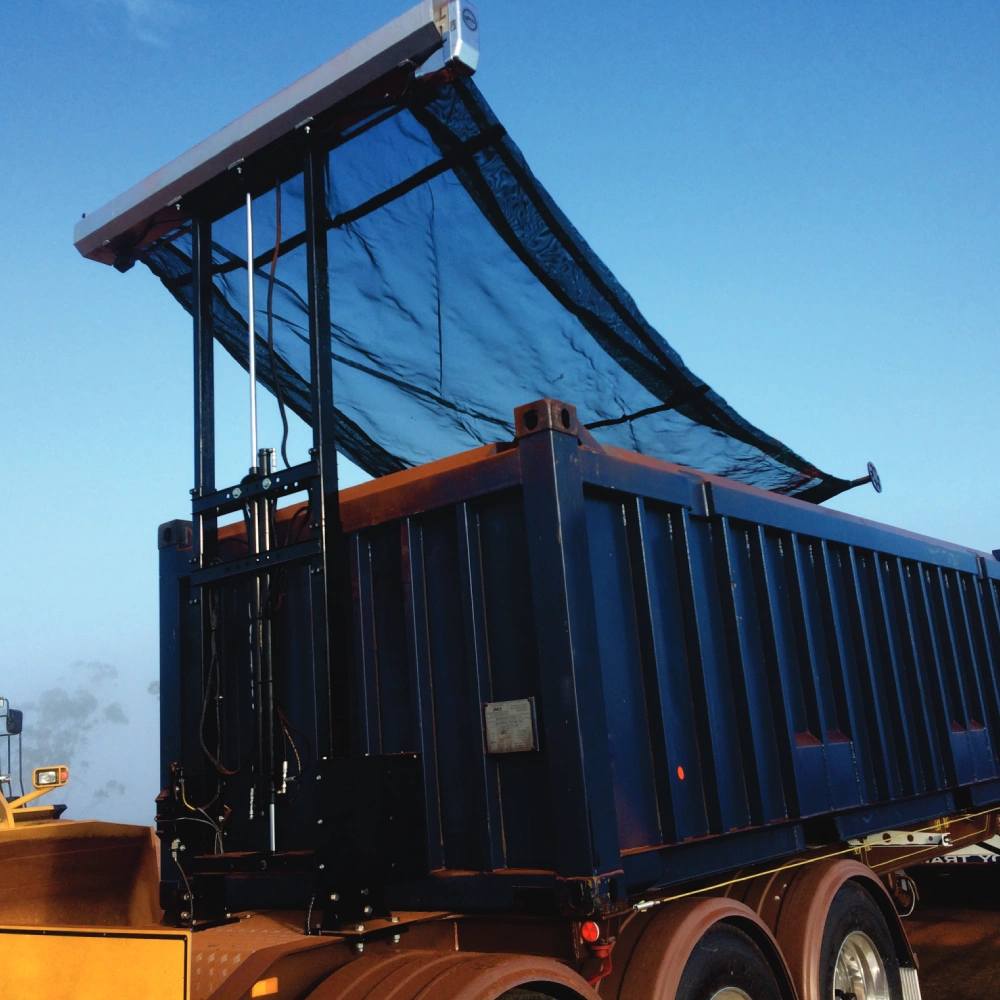Picture of a dump truck depicting the mechanism of the dump tarp in use with a blue sky background.
